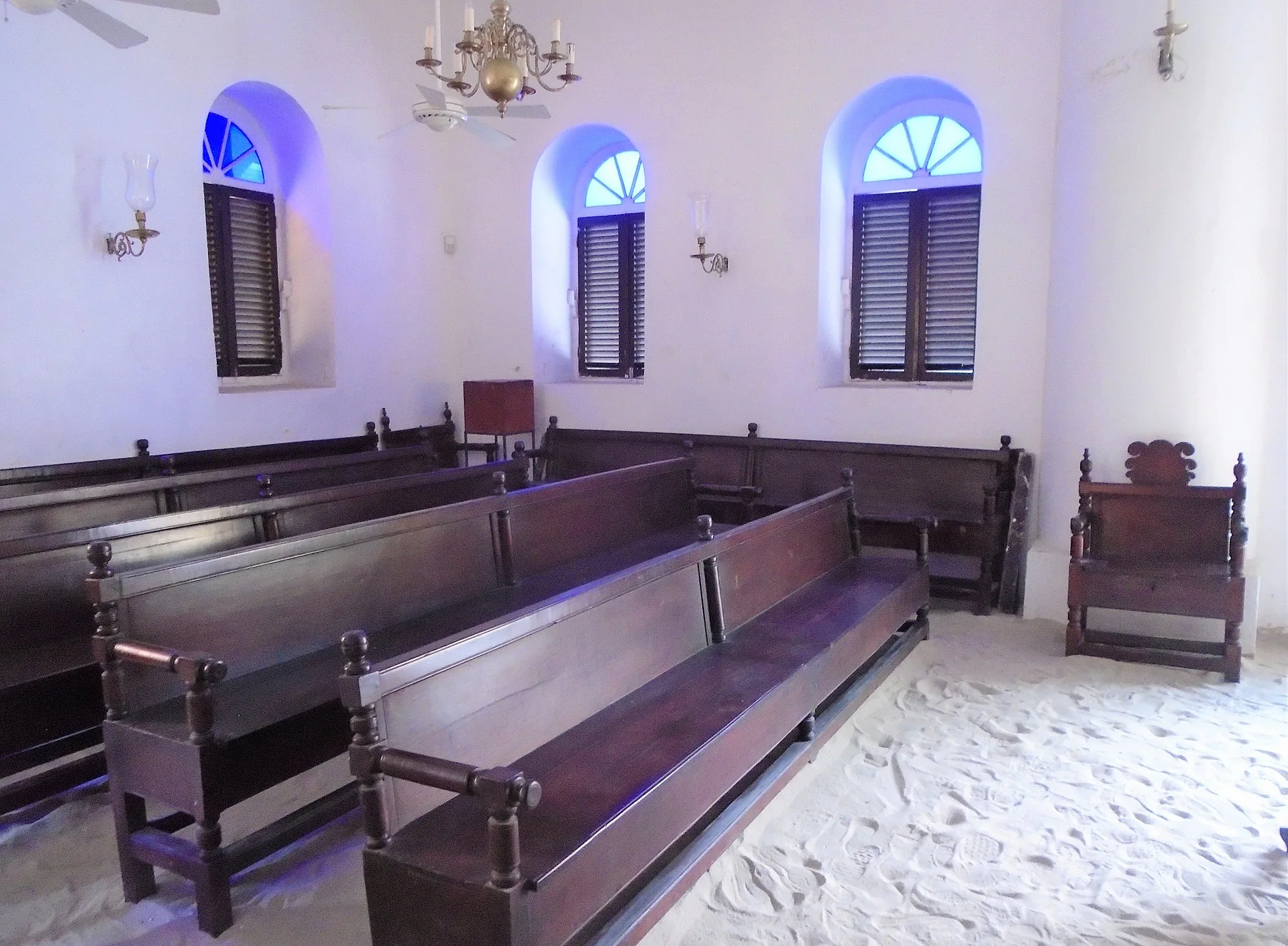 Interieur van de Mikvé Israel-Emanuel synagoge in Willemstad met witte zandvloer, houten banken en messingluchters